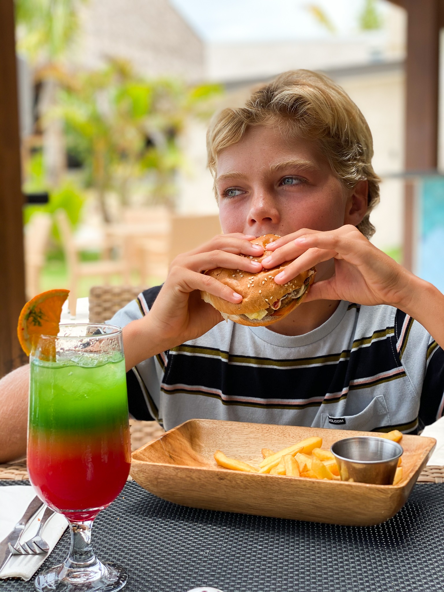 A young man eating hamburger with fries and a ice tea drinks