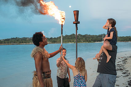 A man in a tribe outfit lighting the torch with children and a man with him.