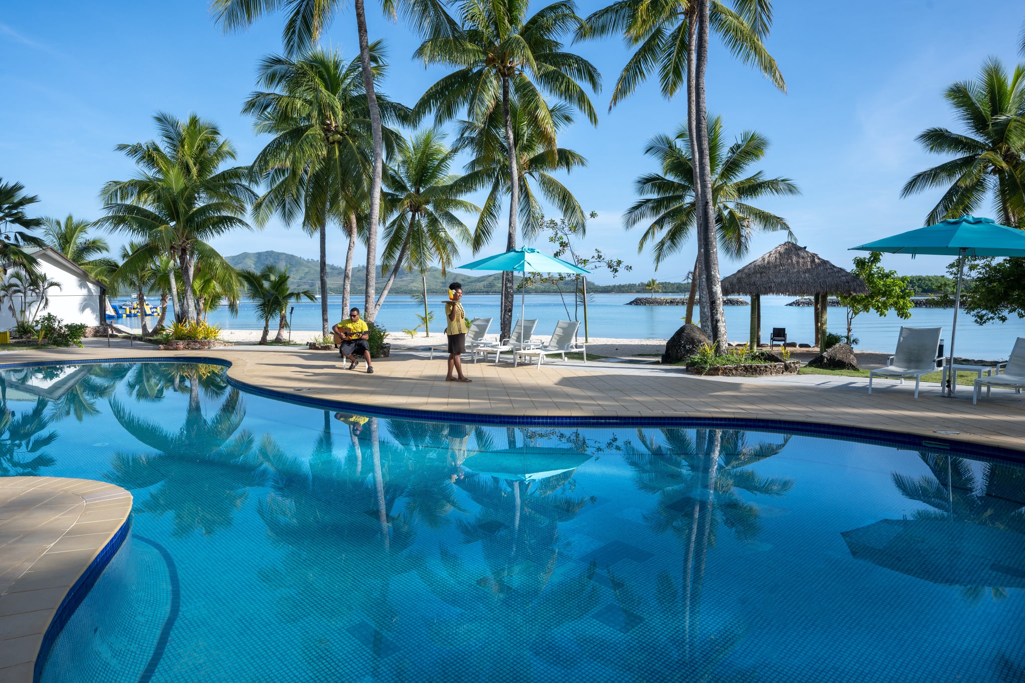 Luxurious swimming pool with a man playing a guitar and a lady serving a drink.