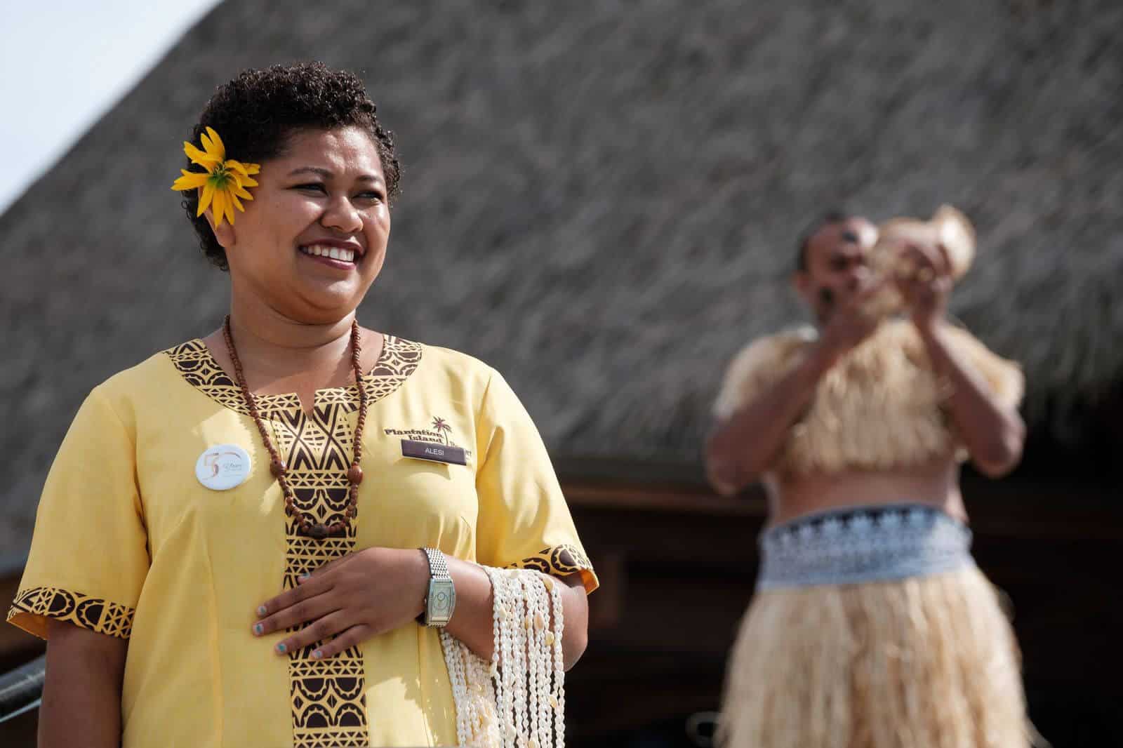 A woman smiling wearing a cultural attire while holding sea shell necklace.